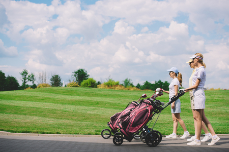 side view of female golfers with golf equipment walking at golf courseの写真素材