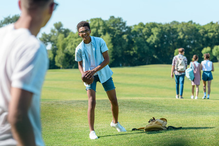 selective focus of multiethnic teenage friends playing with rugby ball in parkの写真素材
