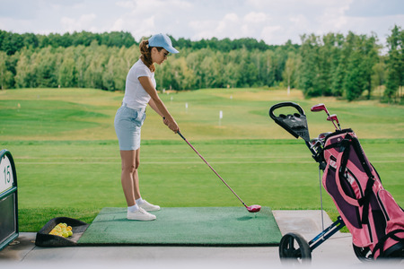 side view of woman in polo and cap playing golf at golf course