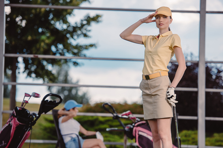 selective focus of female golf player playing golf while friend resting behind at golf courseの写真素材
