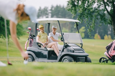 selective focus of woman playing golf while friends riding golf cart at golf courseの写真素材