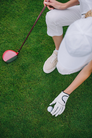 overhead view of woman in cap and golf glove putting ball on green lawn at golf courseの写真素材