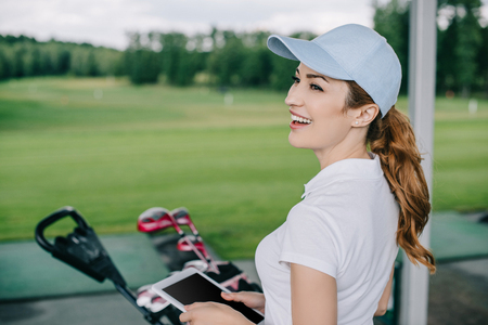side view of cheerful female golf player with tablet in hands at golf courseの写真素材