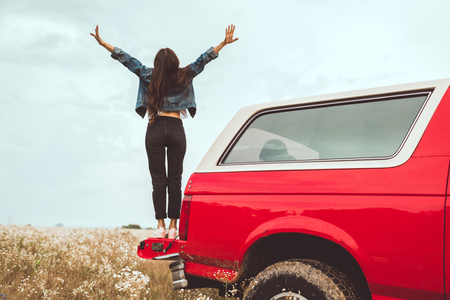 rear view of young woman standing in car trunk in flower fieldの写真素材
