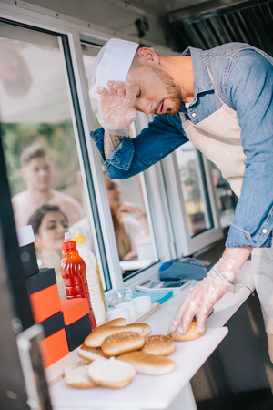 tired chef working in food truck while customers waiting outsideの写真素材