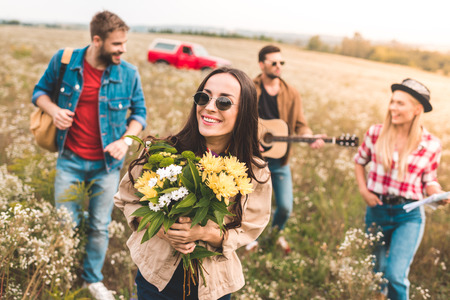 group of young people walking by field with guitar and flower bouquetの写真素材