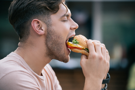 side view of man eating tasty burger with closed eyesの写真素材