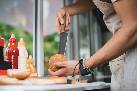 cropped image of chef cutting bun with knife in food truckの写真素材