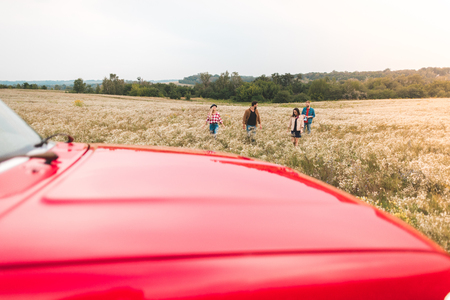 group of young people walking by flower field during car tripの写真素材
