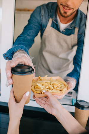 cropped shot of chef giving french fries and coffee to go to client in food truckの写真素材