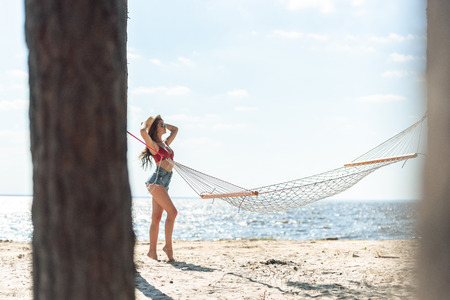 girl in straw hat posing on sea beach with hammock and blue skyの写真素材
