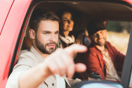 Handsome young man pointing somewhere while riding car with friendsの写真素材