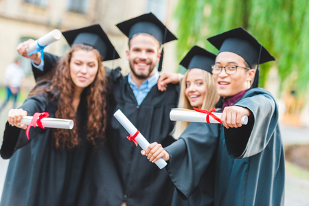 Portrait of happy multiracial graduates with diplomas on streetの写真素材