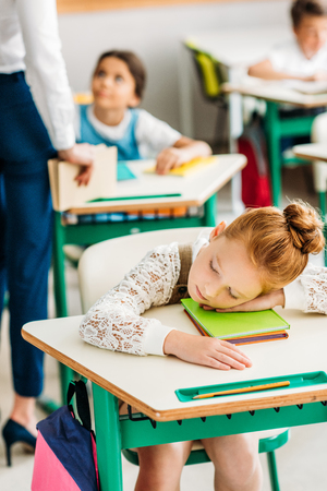 Tired little schoolgirl sleeping on desk during lessonの写真素材