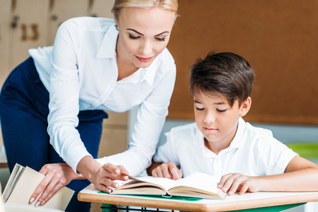 Close-up shot of teacher helping happy schoolboy at classroomの写真素材