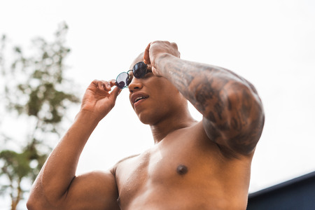 low angle view of muscular tattooed man taking off sunglassesの写真素材