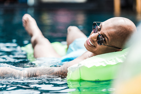 smiling man resting on inflatable mattress looking at camera in swimming poolの写真素材
