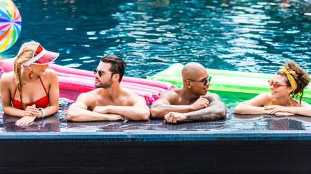 young friends in sunglasses resting in swimming pool near inflatable mattresses