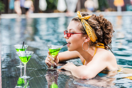 attractive young woman drinking cocktail in swimming poolの写真素材