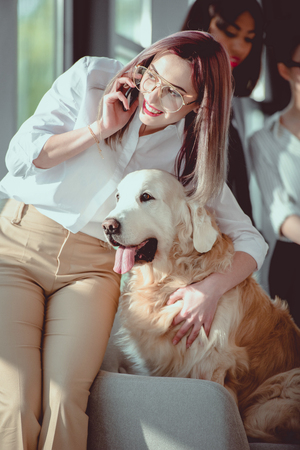 smiling caucasian businesswoman talking on smartphone and hugging dogの写真素材