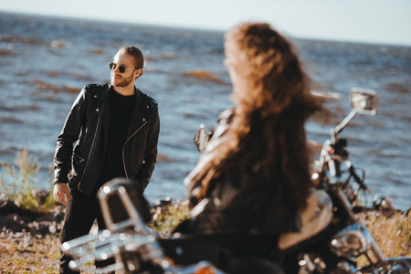 selective focus of girlfriend sitting on vintage motorbike and looking at boyfriend in black leather jacketの写真素材