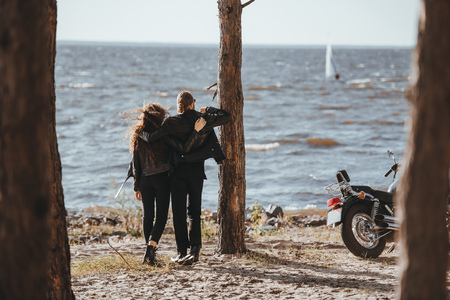 rear view of couple of bikers hugging and looking at sea, motorbike standing nearの写真素材