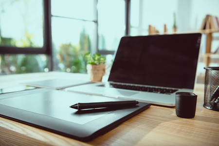 laptop with blank screen and graphics tablet on wooden tabletop at officeの写真素材