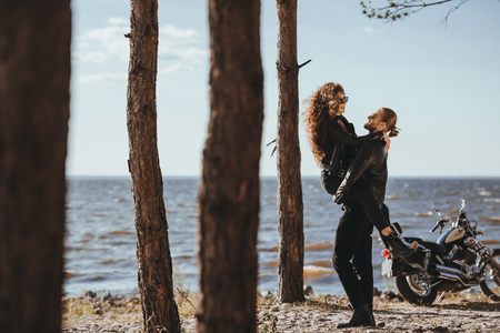 boyfriend holding his happy girlfriend on arms on seashore with motorcycle nearの写真素材