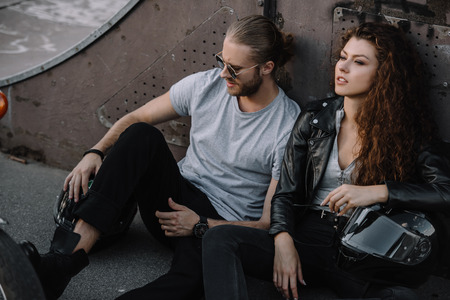 couple of bikers sitting on asphalt with helmets and chopper motorcycleの写真素材