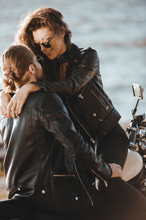 couple of bikers in black leather jackets hugging on motorcycle on seashoreの写真素材