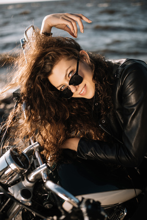 beautiful young woman smiling and sitting on classic motorbikeの写真素材