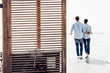 rear view of stylish couple standing on pier near lake at country houseの写真素材