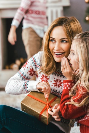 mother and daughter gossiping and unpacking gift together while sitting on floorの写真素材