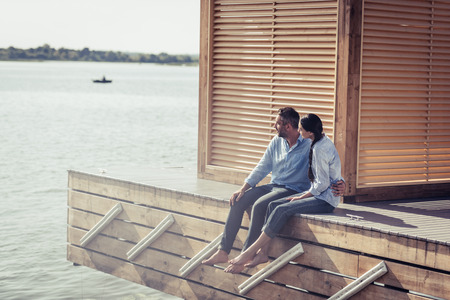 couple embracing each other and sitting on wooden pier near lakeの写真素材