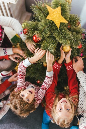 high angle view of kids decorating chrstmas tree with family and looking at cameraの写真素材