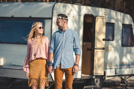 hippie couple looking at each other while holding hands and posing near campervan