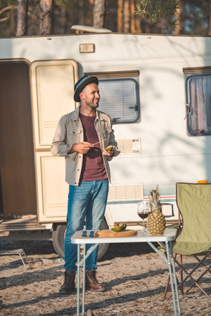 happy man cutting avocado near table with wine and pineapple, vanlife in natureの写真素材