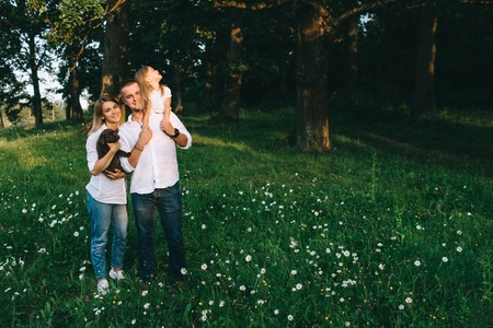 smiling parents with daughter and little labrador puppy in forest