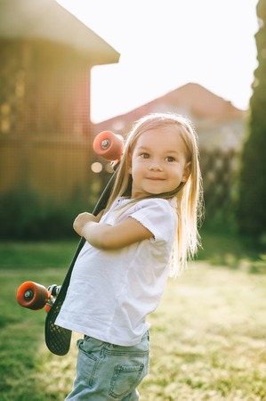 portrait of smiling adorable little skater with penny board in hands on yardの写真素材