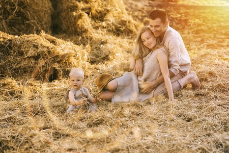 parents and little son in linen clothing resting on hay at countrysideの写真素材