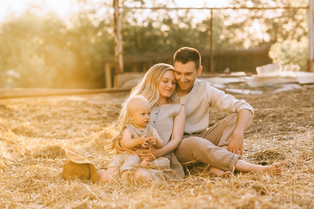 family with little son in linen clothing resting on hay at countrysideの写真素材