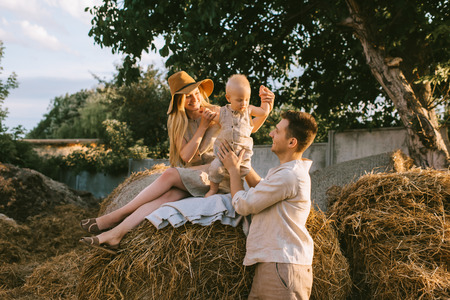 family with little son in linen clothing resting on hay at countrysideの写真素材