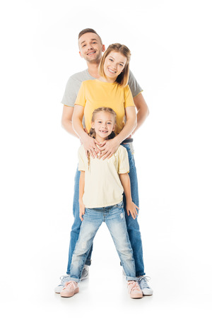 smiling parents and little daughter hugging each other and looking at camera isolated on whiteの写真素材