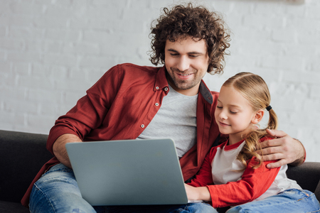 happy father and daughter using laptop together at homeの写真素材