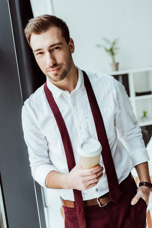 handsome businessman with disposable cup of coffee in officeの写真素材