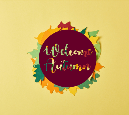flat lay with colorful papercrafted foliage with "welcome autumn" lettering in circle on yellow backgroundの写真素材