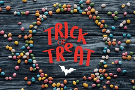 circle made of colorful delicious candies on wooden background with bat and trick or treat lettering