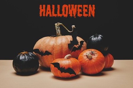 orange and black pumpkins with paper bats on table with halloween sign
