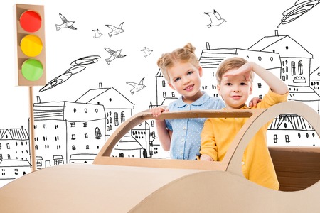 siblings playing with cardboard car and traffic lights in drawn city with birdsの写真素材