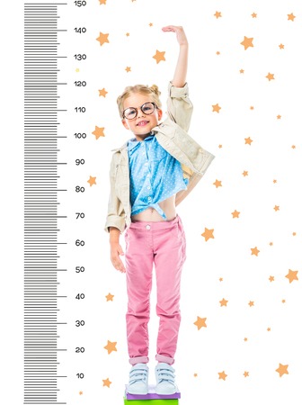 happy kid in eyeglasses standing on pile of books to be higher isolated on white with stars and growth measuresの写真素材